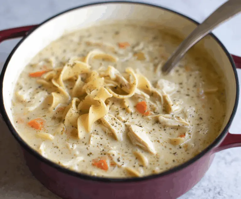 Creamy chicken noodle soup in a bowl with tender chicken, vegetables, and creamy broth, garnished with fresh herbs, served hot.