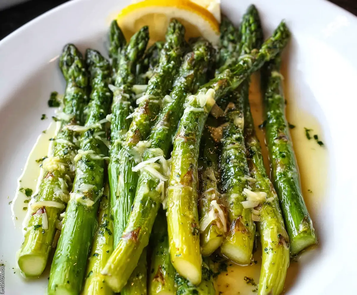 Delicious Lemon Butter Asparagus on a white plate, garnished with fresh lemon slices and herbs.
