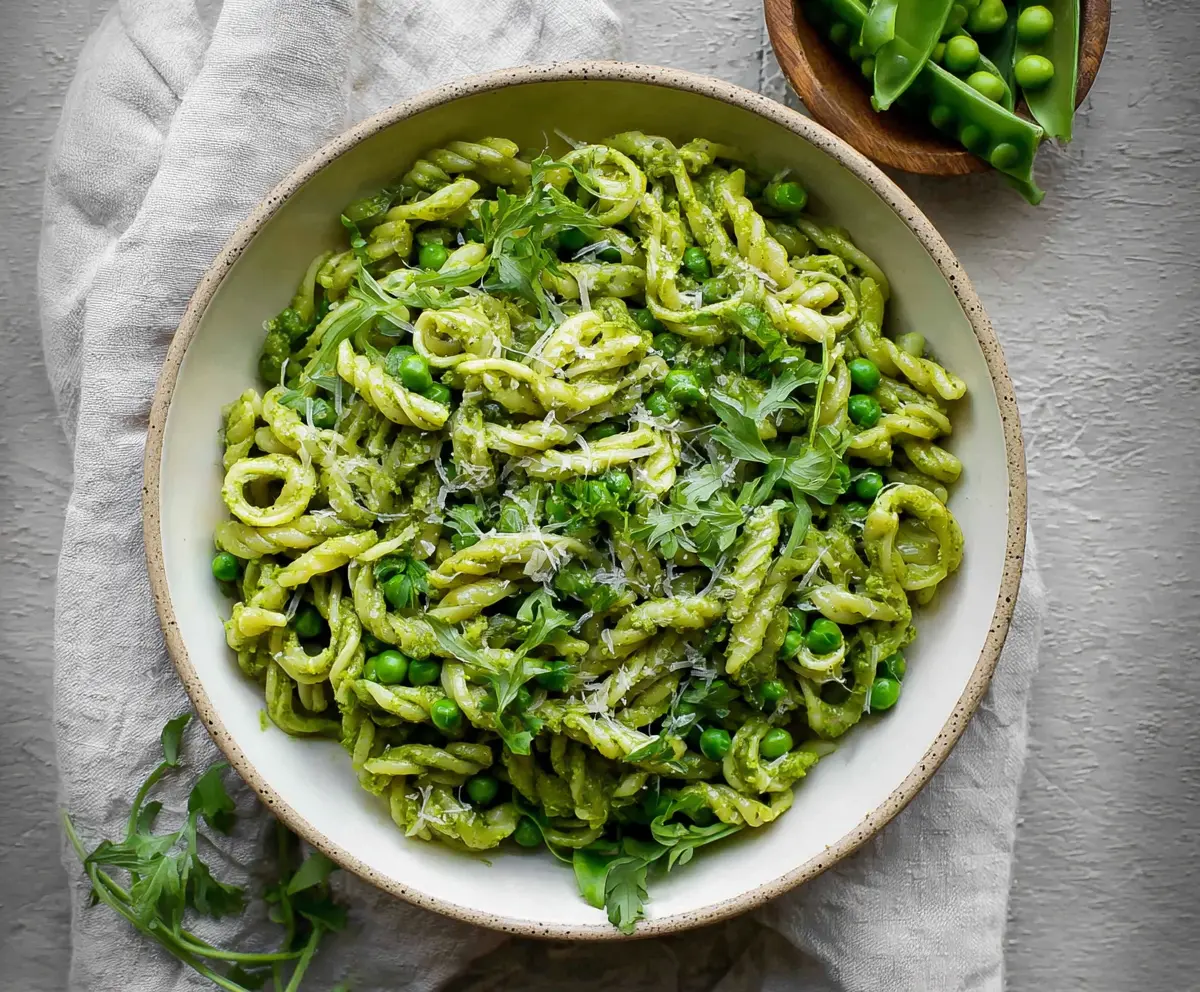 Creamy spring pea pesto pasta served with fresh herbs and grated cheese.